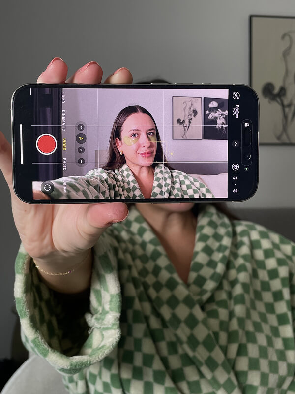 Emily holding up a phone filming herself in a green checked robe