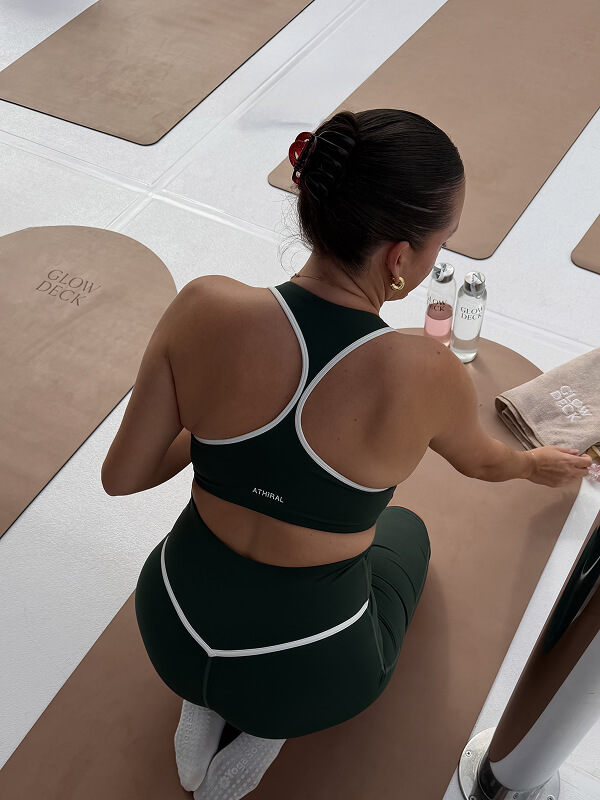 Emily kneeling on a mat at a pilates studio in a green Athiral set